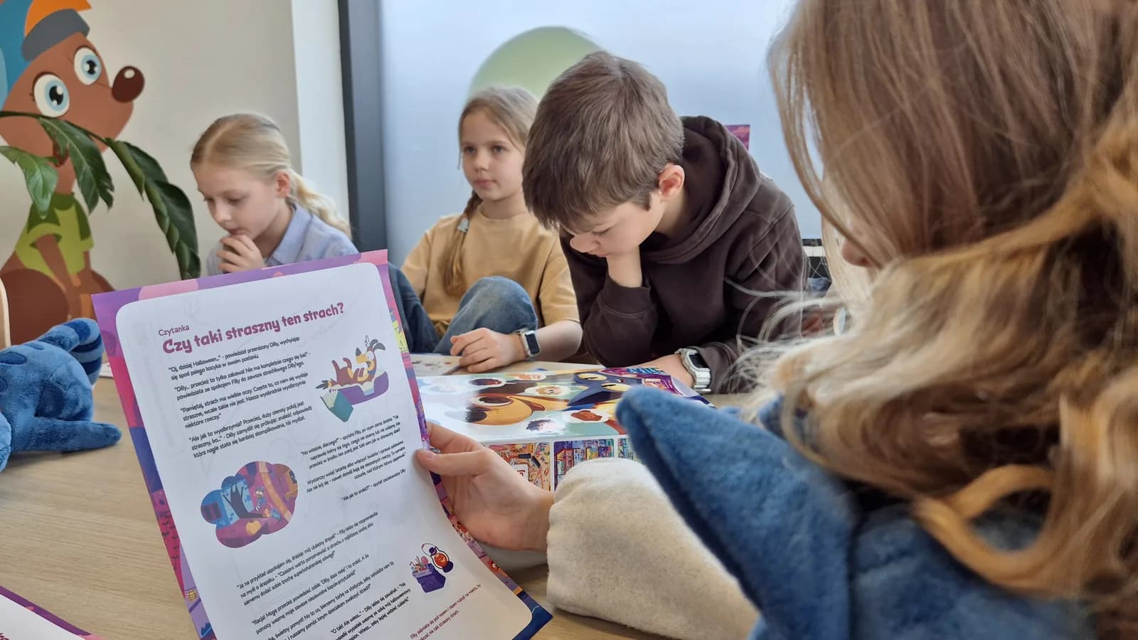 Nauczycielka pokazuje kartę o strachu, dzieci słuchają przy stole