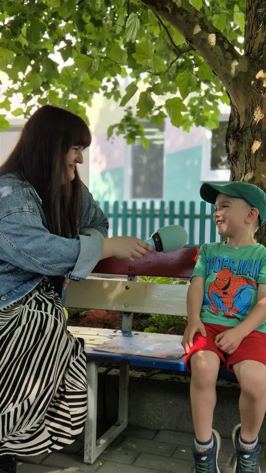 Nauczycielka rozmawia z chłopcem na ławce, trzymając zabawkowy mikrofon